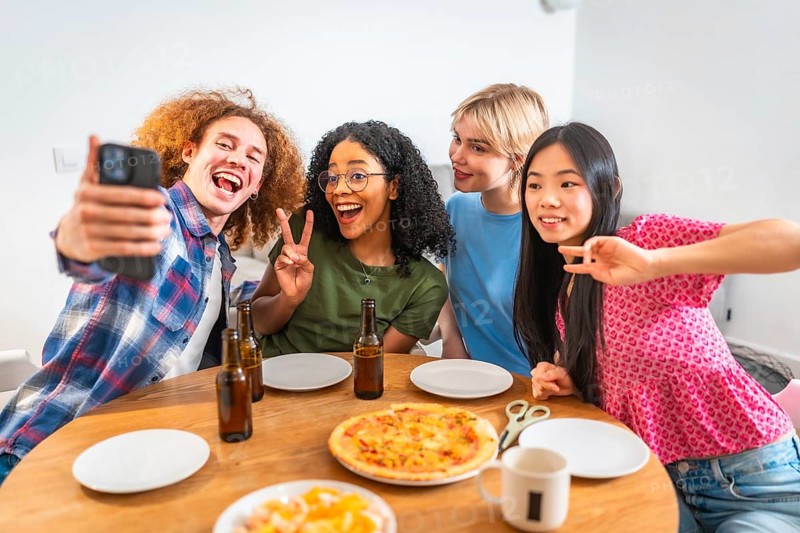 Four diverse friends are taking a selfie while enjoying pizza and beer, celebrating friendship and togetherness