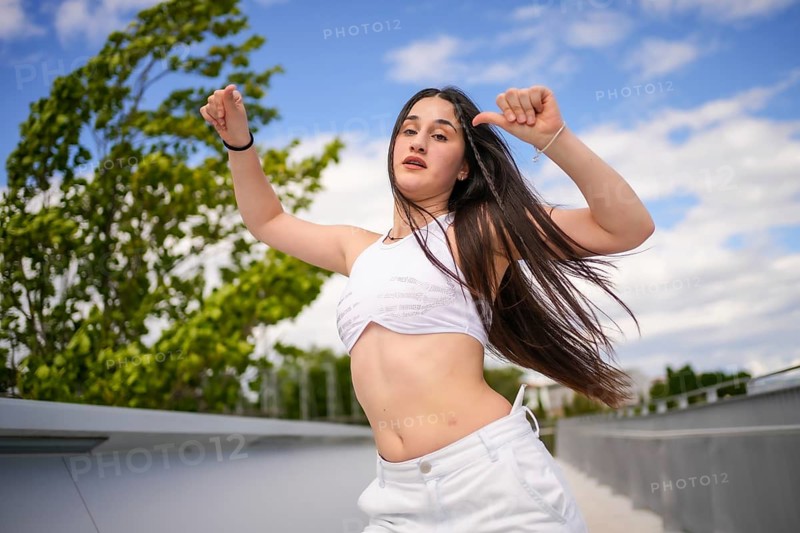 Young caucasian woman with arms raised and tousled hair dancing freestyle on an urban park