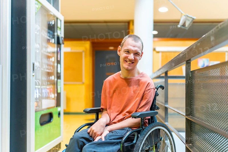 Caucasian smiling man with cerebral palsy next to a vending machine in a modern coworking