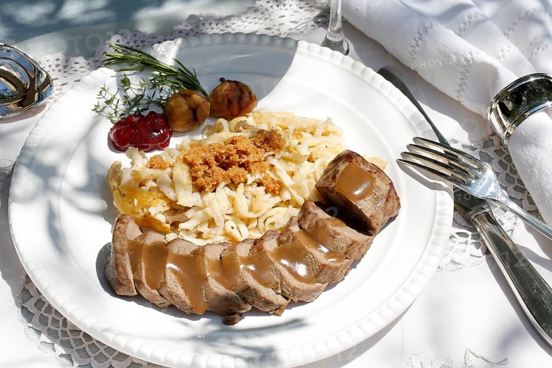 Swabian cuisine, roast venison with spaetzle, chestnuts and breadcrumbs, breadcrumbs, saddle of venison arranged on a plate, gravy, game dish, meat, main course, gravy, cutlery, knife, fork, grandmother's kitchen, regional, home cooking, typical Swabian, traditional cuisine, festive tablecloth, food photography, studio, Germany, Europe