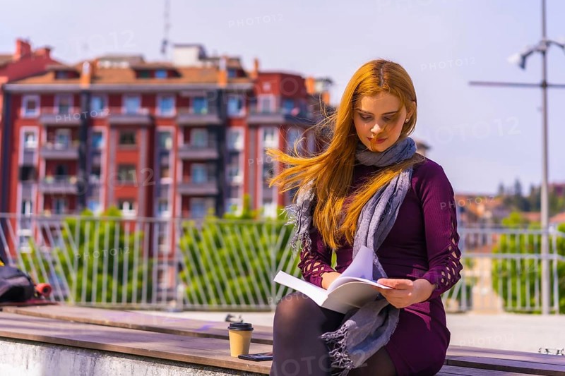 Beautiful woman in purple dress and scarf reading a book in a park in the city, imagining and enjoying reading