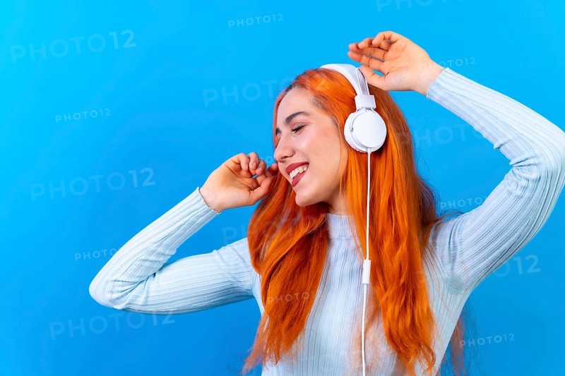 Redhead woman in studio photography smiling dancing on a blue background