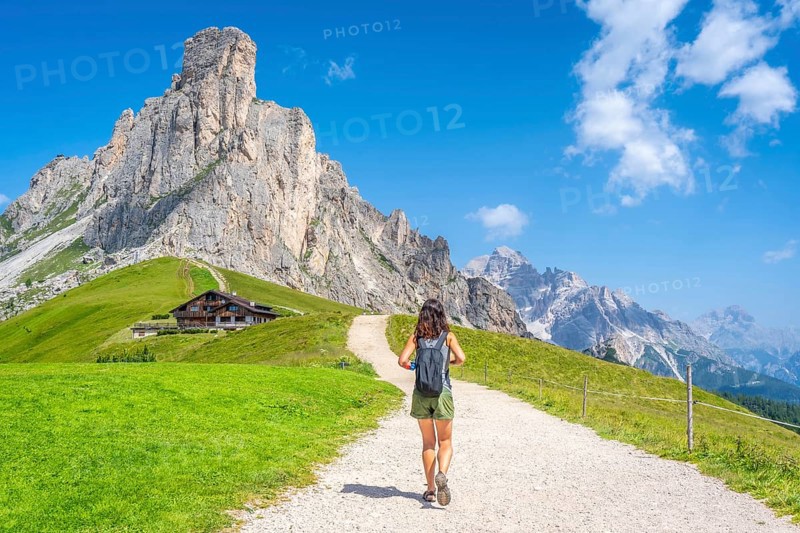 Female tourist walking on a gravel path enjoying the view of the nuvolau peak and the mountain shelter near giau pass in the italian dolomites