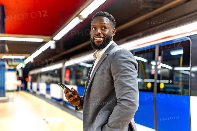 Young businessman waiting for a subway train, using his smartphone to check messages and browse social media while on the platform