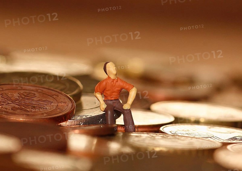 Miniature man sitting among euro coins, North Rhine-Westphalia, Germany, Europe