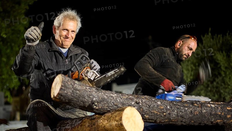 ©Udo Rein, An elderly man gives a thumbs up while sitting next to a woodworker with a chainsaw, Easter bonfire Psinthos, Holy Saturday, Easter, Psinthos, Rhodes, Dodecanese, Greek Islands, Greece, Europe