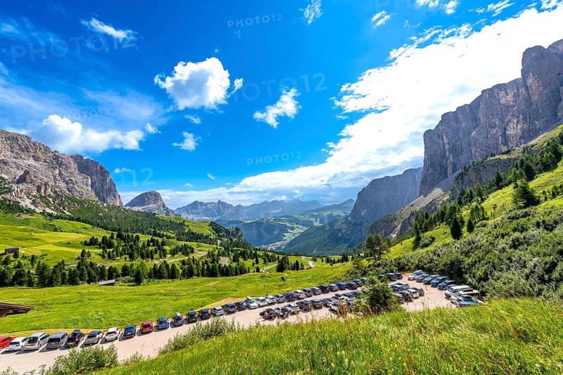 Cars parked near gardena pass with breathtaking views of the dolomites mountains in a sunny summer day