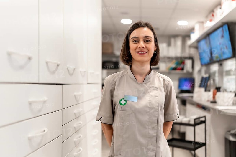 Young and proud female pharmacist standing with arms in the back in the storage room in a modern shop