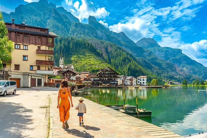 Tourists strolling along the lakefront of alleghe, a charming village nestled in the heart of the italian dolomites, enjoying the stunning mountain scenery on a summer day