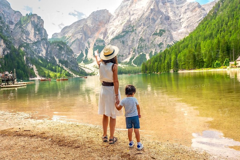 Mother pointing at the landscape while holding her son's hand on the shore of lake braies in the italian dolomites during summer