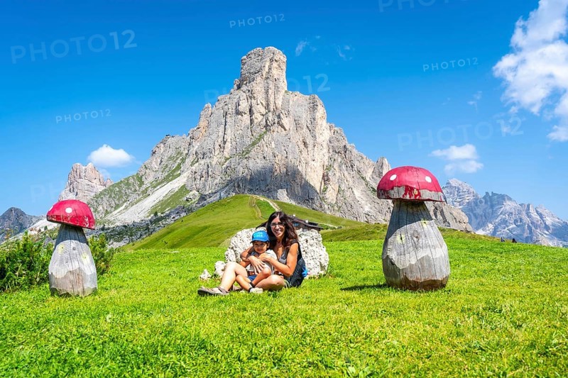 Mother and child are resting near wooden mushrooms at giau pass, a high mountain pass in the dolomites, italy