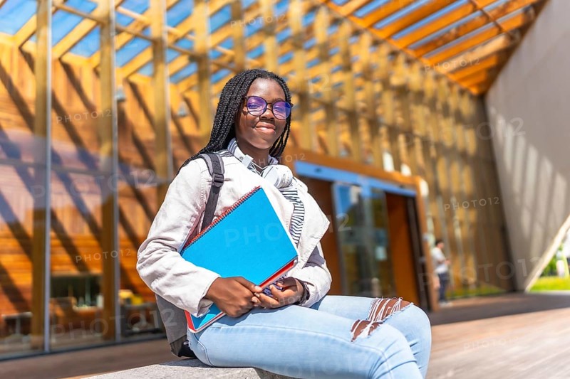Female african student sitting outside the university and smiling at camera in a sunny day