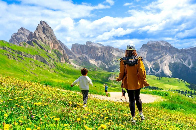 Tourists enjoying a sunny summer day walking through fields of wildflowers in seceda, dolomites, italy