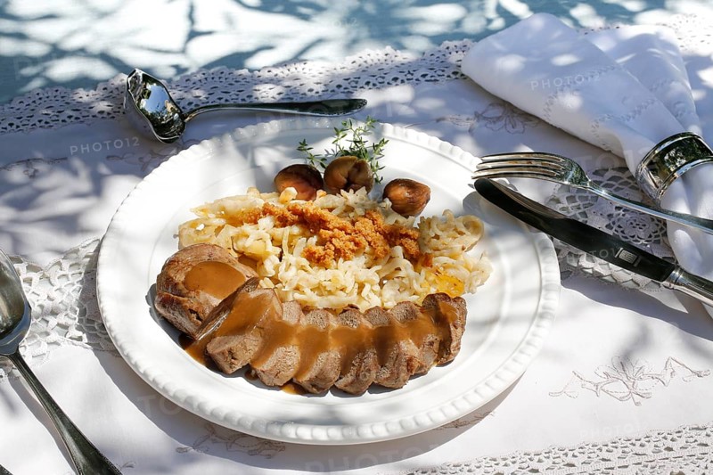 Swabian cuisine, roast venison with spaetzle, chestnuts and breadcrumbs, breadcrumbs, saddle of venison arranged on a plate, gravy, game dish, meat, main course, gravy, cutlery, knife, fork, grandmother's kitchen, regional, home cooking, typical Swabian, traditional cuisine, festive tablecloth, food photography, studio, Germany, Europe
