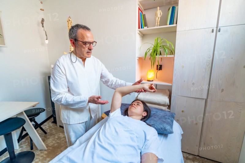 Qi gong masseur performing massage and stretching to a patient lying on stretcher in a clinic
