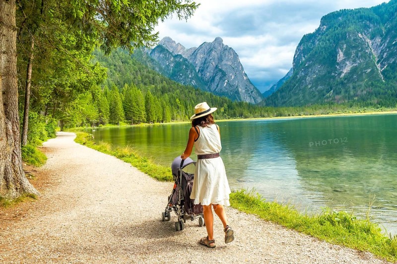 Tourist walking with her baby along the scenic shores of lake dobbiaco, surrounded by the stunning dolomite peaks in italy