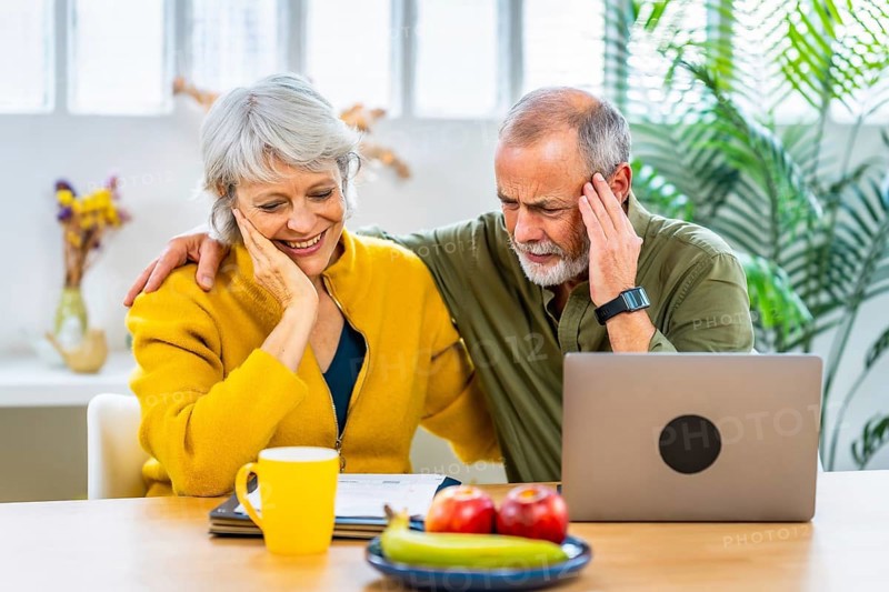 Senior couple doing accountability at home sitting using laptop and expressing happiness