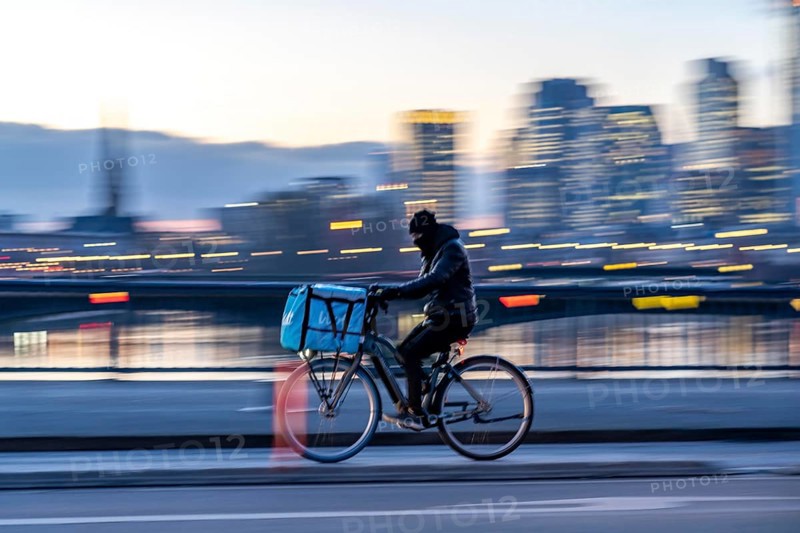 Skyline of the city centre of Frankfurt am Main, cyclist on the Flößerbrücke, Wolt delivery service, dusk, river Main, winter, Hesse, Germany, Europe
