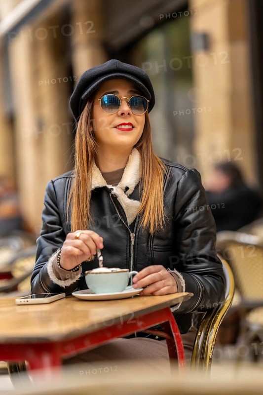 Fashionable woman wearing sunglasses and a hat savoring a cappuccino at a parisian cafe, enjoying the european atmosphere