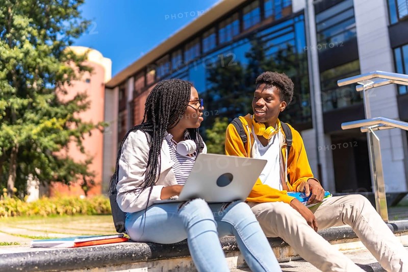 Two african american students using laptop sitting on the campus