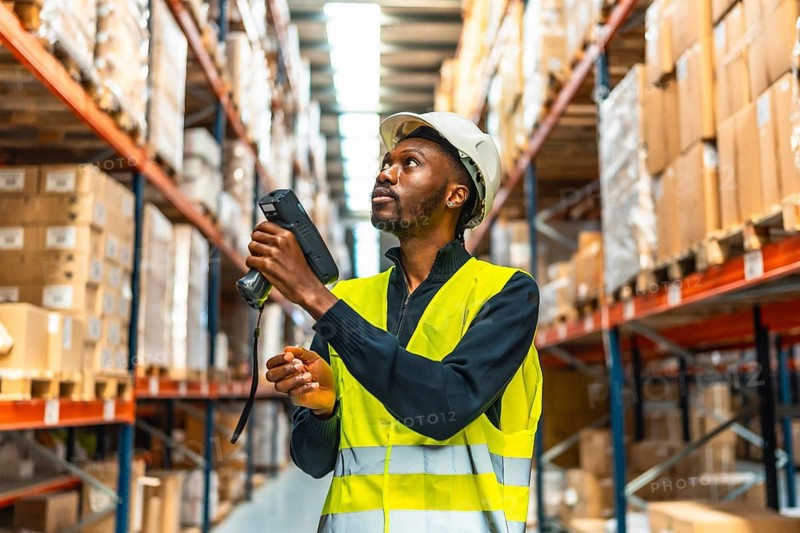 African american manual worker in reflective clothes scanning parcels in a warehouse full of boxes