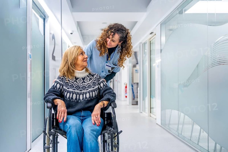 Young tender nurse talking to a mature injured woman in wheelchair in the hospital