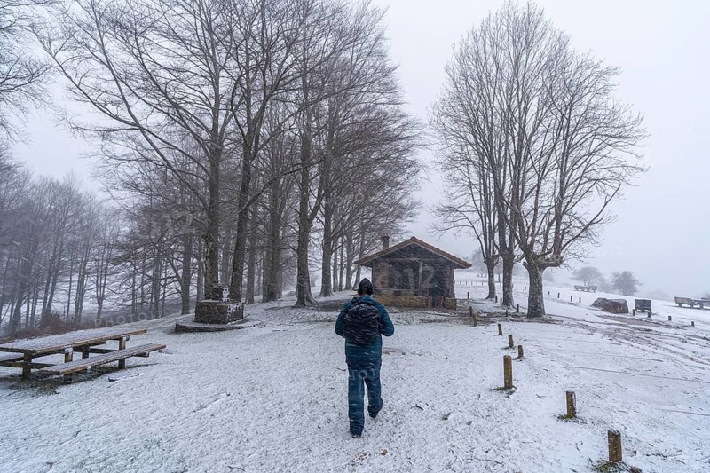 A young man walking next to the refuge of mount aizkorri in gipuzkoa. Snowy landscape by winter snows. Basque Country, Spain, Europe