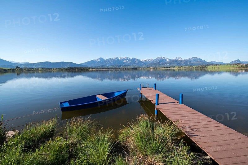 Blue sky over an alpine lake with a boat and a jetty, surrounded by mountains, Hopfen am See, near Füssen, Ostallgäu district, Swabia, Bavaria, Germany, Europe