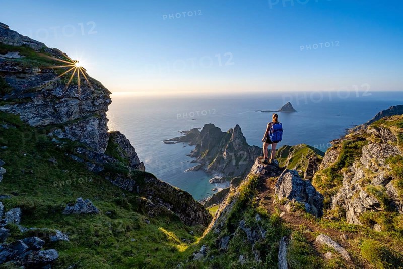 Mountaineer on the summit of Måtind or Måtinden, view of picturesque coastal landscape with sun star, rocky coast and sea, Andøya Island, Vesterålen, Nordland, Norway, Europe