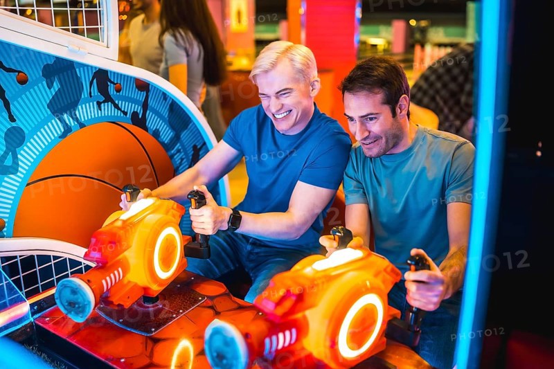 Two male friends enjoying their free time playing arcade basketball simulator together, laughing and having fun