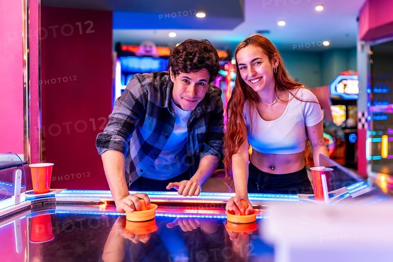 Multiethnic friends having fun together playing air hockey in a colorful amusement arcade