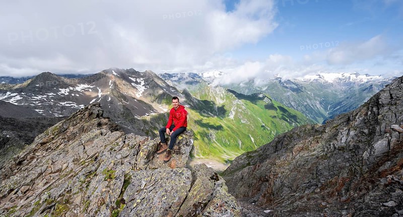 Mountaineer sitting on a rock, on a steep rocky ridge, on the summit of the Lasörling, view of the mountain panorama of the Venediger Group, Lasörling Group, Hohe Tauern National Park, East Tyrol, Tyrol, Austria, Europe