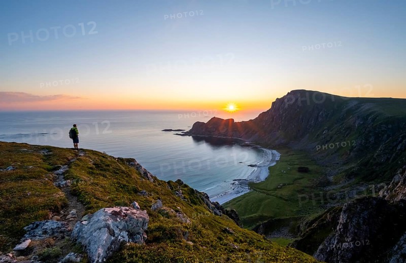 Mountaineer in front of view of coastal landscape at sunset, cliffs and summit of Måtind or Måtinden, Høyvika beach and sea, Andøya island, Vesterålen, Nordland Norway