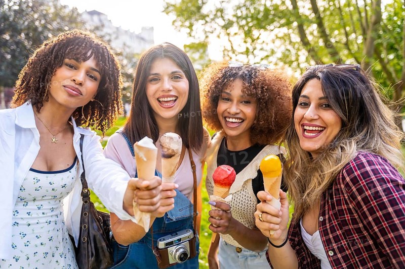 Four cheerful young women enjoying ice cream cones together in a park, celebrating friendship and summer vibes