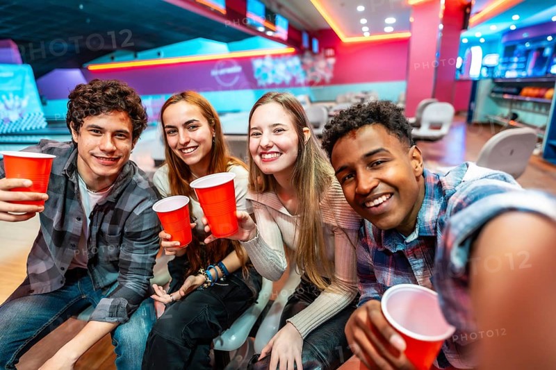 Group of cheerful young multiethnic friends taking a selfie while drinking and having fun in a bowling club
