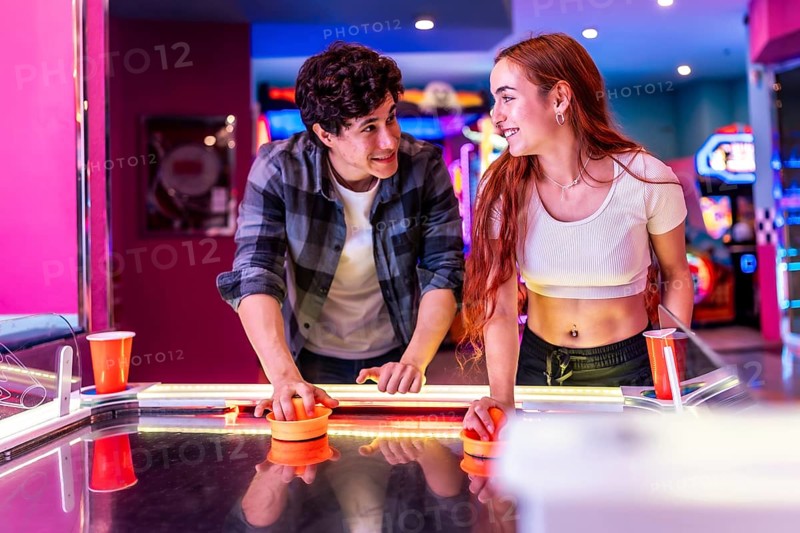 Happy multiethnic friends enjoying a weekend together, playing air hockey in a colorful and dynamic arcade