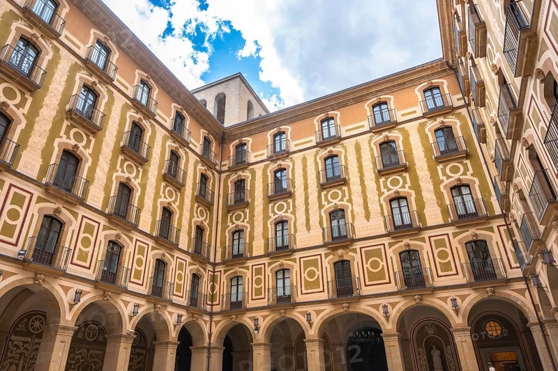 Low angle view of the courtyard of montserrat monastery, showing arched walls, balconies, and decorative facade on a sunny day
