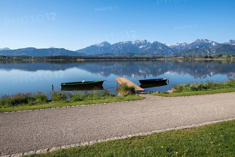 Calm lake with green and black boats, jetty and alpine landscape in the background, Hopfen am See, near Füssen, Ostallgäu district, Swabia, Bavaria, Germany, Europe