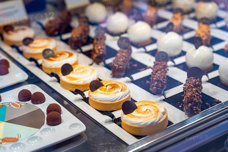 Mouth watering pastries and small cakes are neatly arranged on display in a bakery window, tempting customers with their sweet appeal