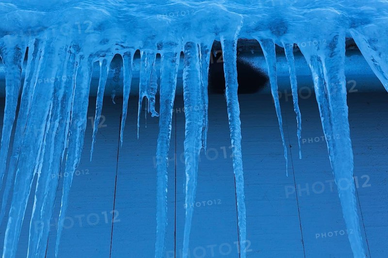 Long icicles and thick heavy ice hanging from roof edge of grey wood plank cladded building in winter, Quebec, Canada, North America