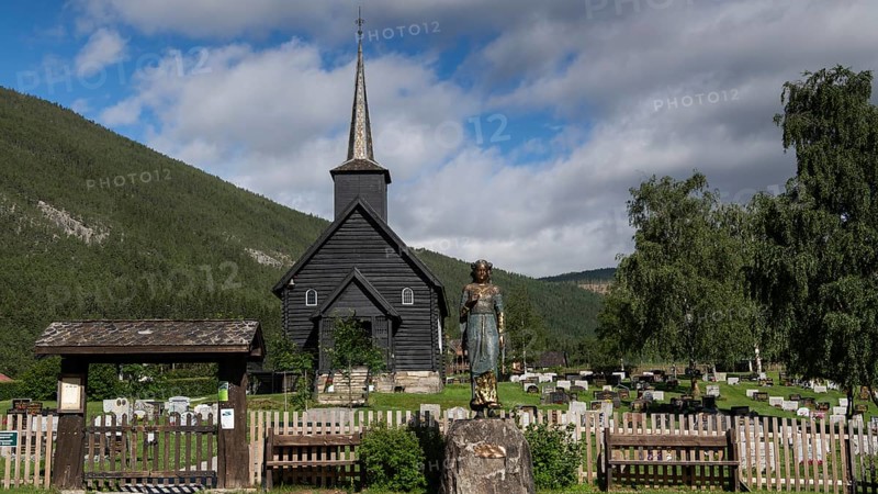 Wooden church in Sel with a cemetery and a statue of Kristian Lavranstochter, the main character from the novel of the same name by Nobel Prize winner Sigrid Undset, in front of a mountainous landscape, Olavsweg or Olavsleden, Sel municipality, Gudbrandsdalen, Norway, Europe