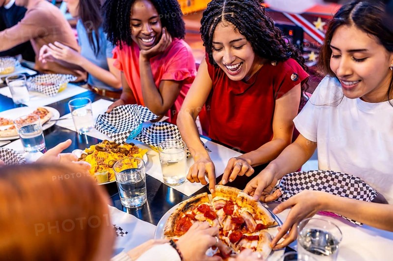 Cheerful multi ethnic friends enjoying pizza and nachos at a bowling alley restaurant, celebrating friendship and leisure time together