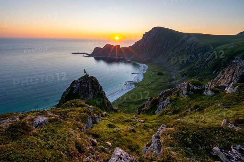 Climber on rocks in front of picturesque landscape, view of coastal landscape at sunset, cliffs and summit of Måtind or Måtinden, Høyvika beach and sea, Andøya island, Vesterålen, Nordland Norway