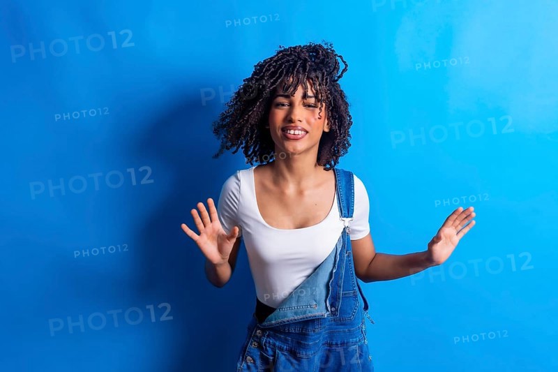 Young woman with curly hair dancing joyfully against a vibrant blue backdrop, embodying carefree energy and youthful expression in a studio setting