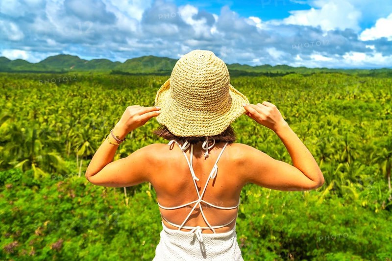Young woman enjoying the view of a wide coconut plantation in siargao island, philippines, holding her straw hat