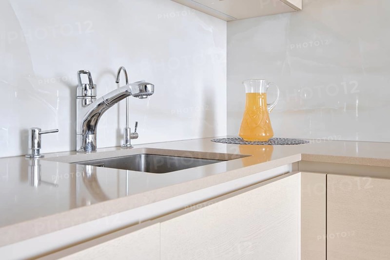 A contemporary kitchen features a polished stone countertop with a shiny faucet and a glass pitcher filled with a refreshing drink. The clean lines and light colours create a bright atmosphere