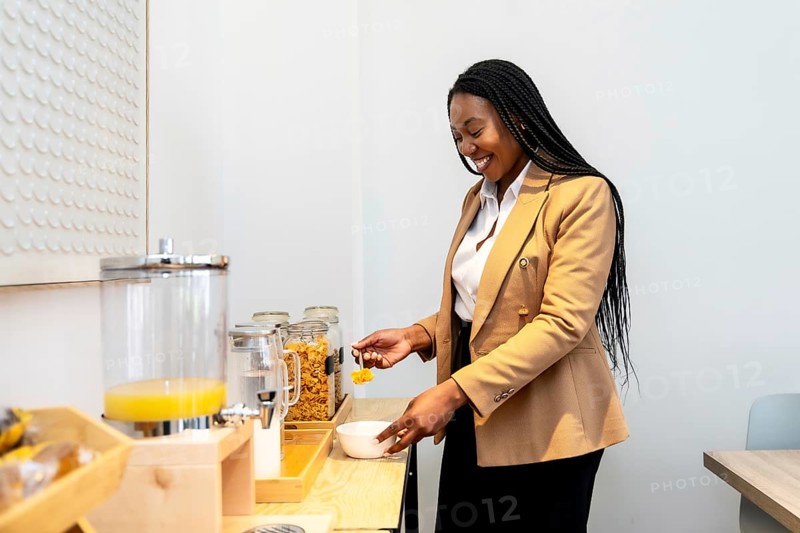 Smiling businesswoman serving breakfast from hotel buffet during business trip, enjoying orange juice and cereals