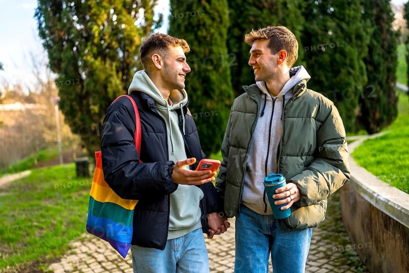 Happy gay couple holding hands and walking in a park, enjoying a relaxing day together and showing love and support for lgbtq plus community
