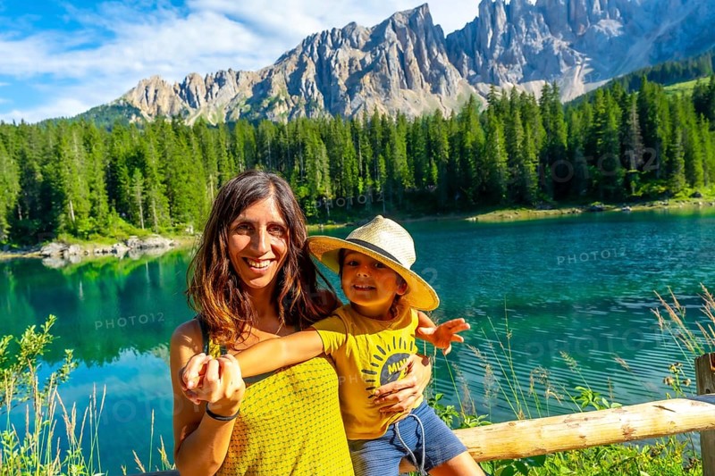 Mother and son smiling and enjoying summer holidays at lake carezza with the latemar mountain range in the background
