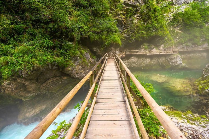 Scenic view of a wooden footbridge spanning a crystal clear emerald river flowing through the picturesque vintgar gorge near bled, slovenia